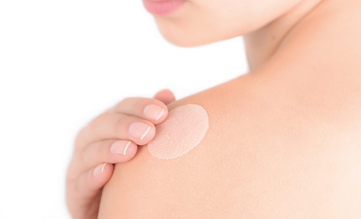 A person applying a clear silicone sheet to their shoulder for scar management.